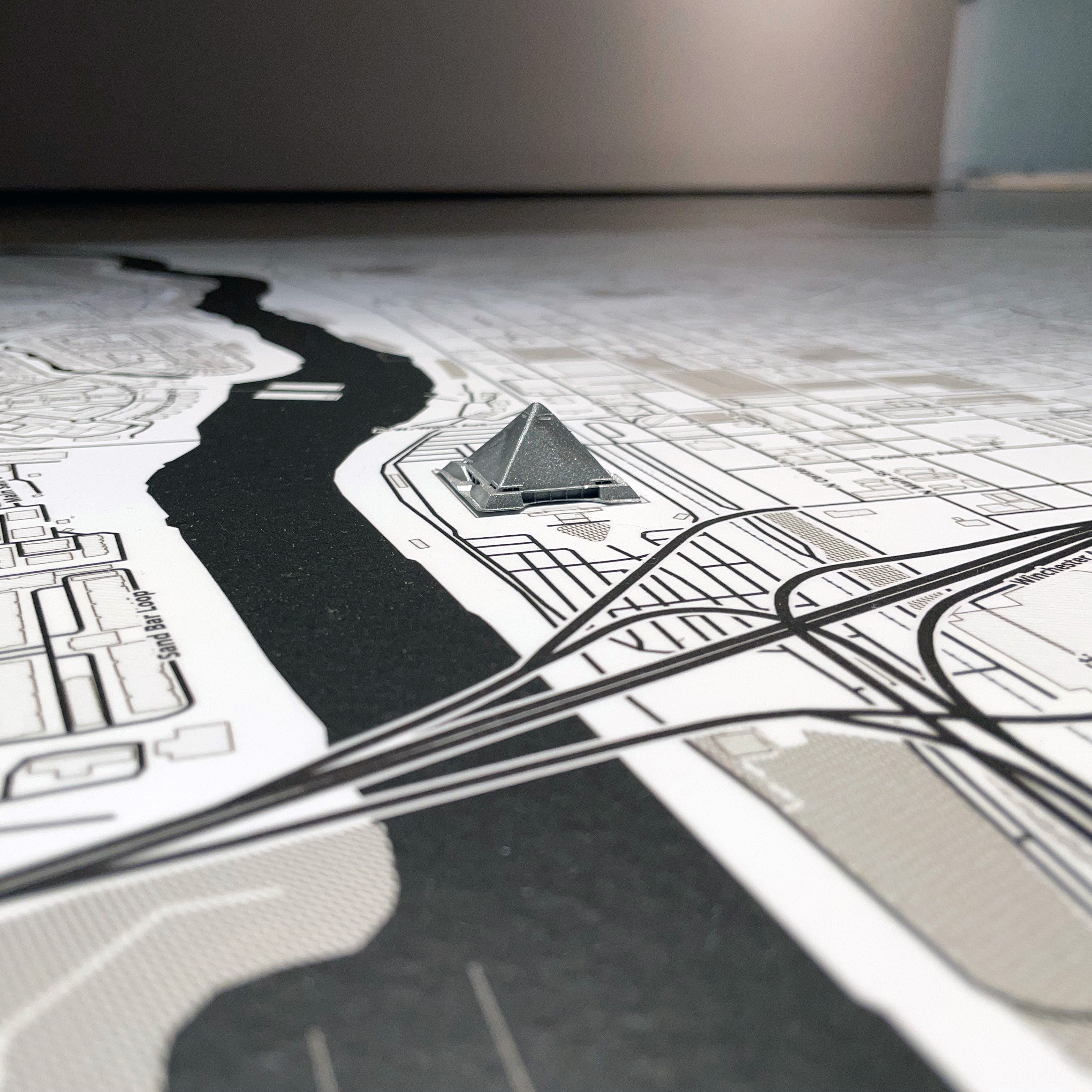 Vinyl black and white map measuring approximately 4 feet by 4 feet. The map is of 
          Memphis neighborhoods including Uptown, Winchester Park, Speedway Terrace, 
          Snowden, Crosstown, and Medical District. Map is adhered to floor. There is a small 
          silver 3D printed pyramid placed atop where the Memphis Pyramid building is located on
          the map.